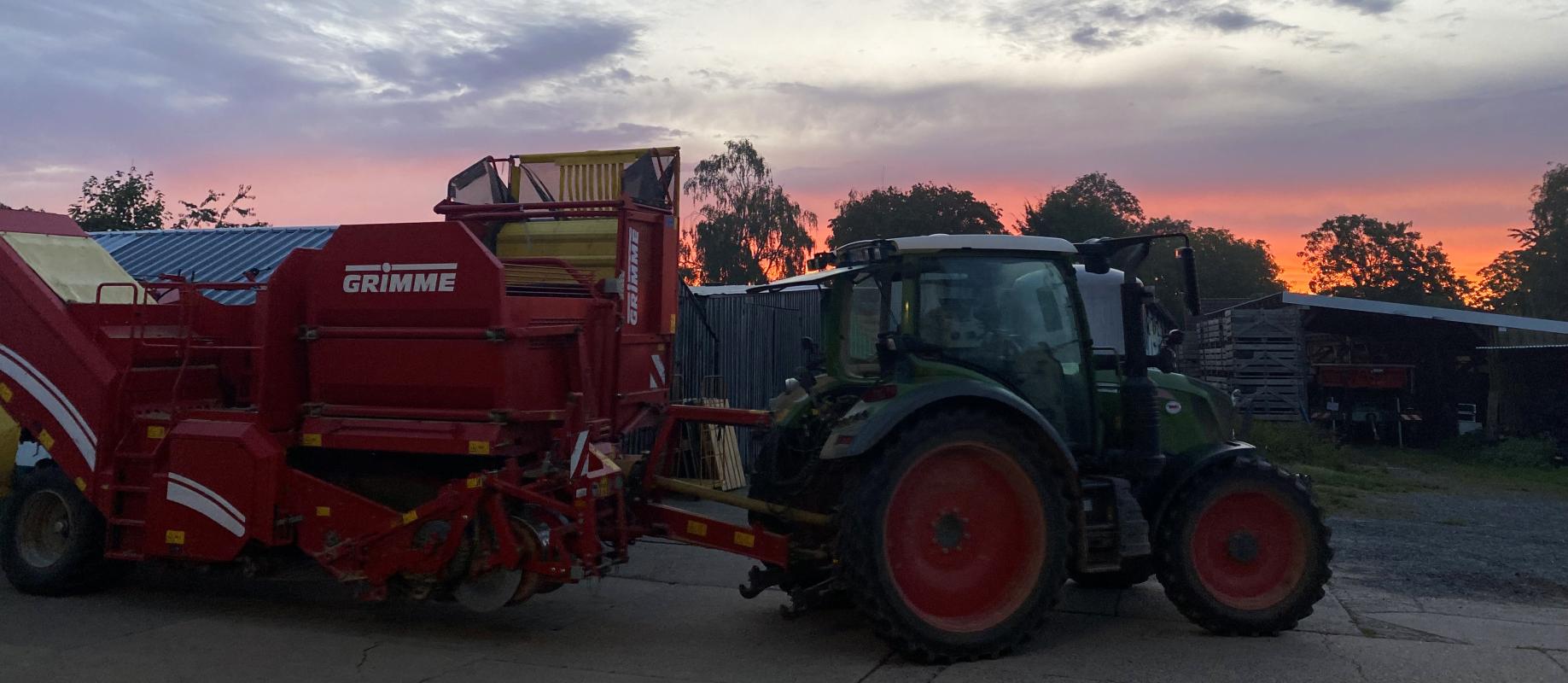 Traktor und Kartoffelroder im Sonnenaufgang